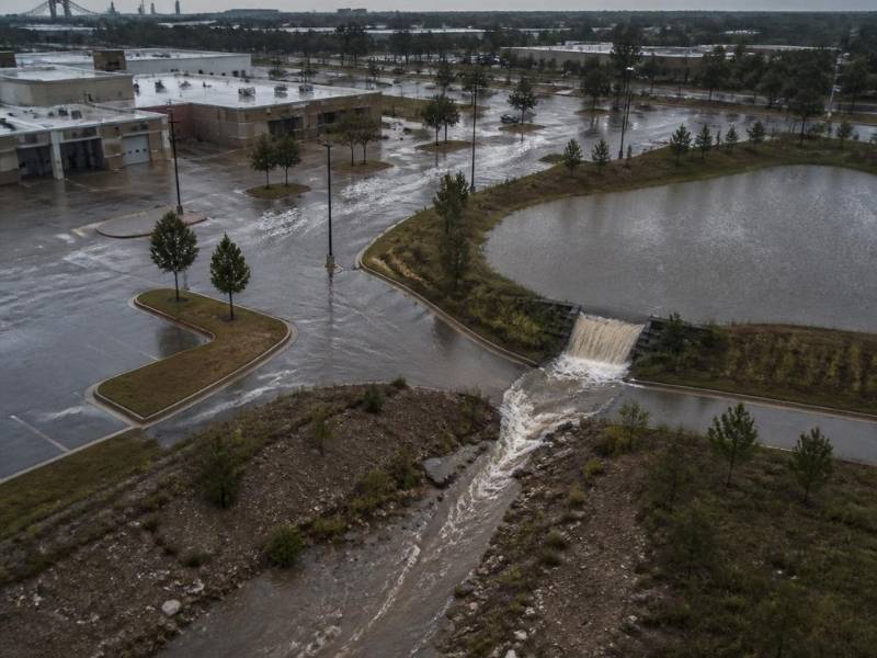 Aerial view of a Memphis commercial site during heavy rainfall with a full detention pond, flooded pavement and a controlled overflow channel.
