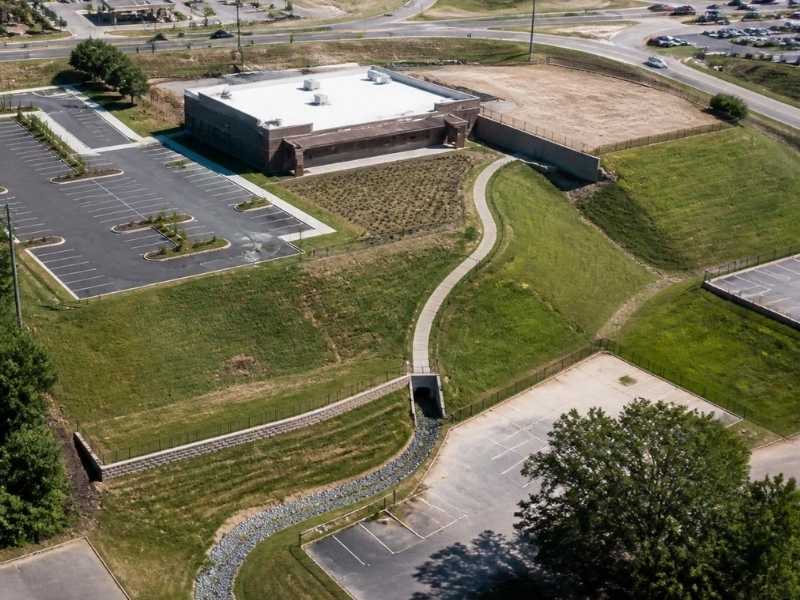 Civil engineer in Memphis, Tennessee, reviewing grades beside an accessible walkway, retaining wall and drainage swale on a sloped commercial site.
